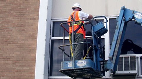 A technician in a boom lift inspecting a building facade at window level.