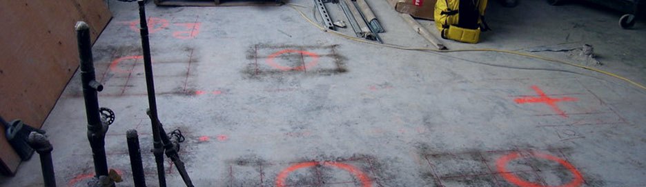 A concrete slab marked in orange paint with circles and crosses showing cleared core locations and reinforcement positions.